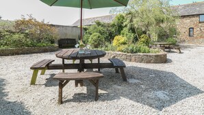An outdoor patio with a wooden table and benches, a green umbrella, and a stone wall. - The Dairy (Bude)