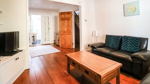 Ein modernes Wohnzimmer mit Couchtisch aus Holz, einer schwarzen Ledersofa mit gemusterten Kissen, einem Flachbildfernseher auf einem weißen Schrank und einer Holztür, die in einen anderen Raum führt.