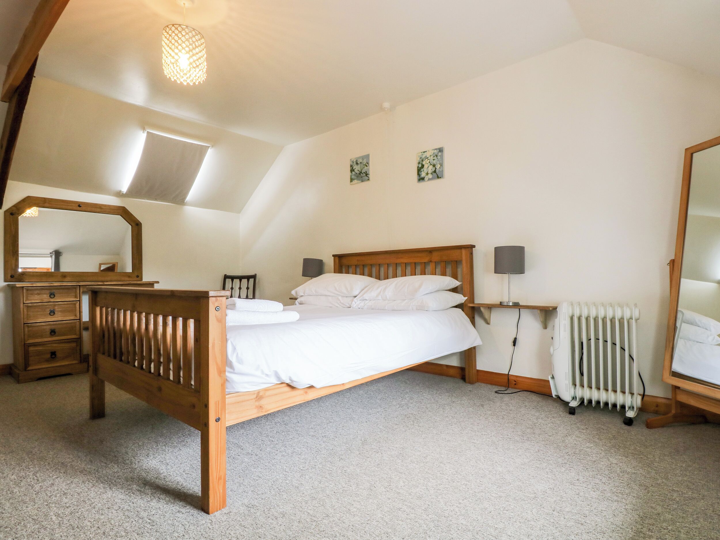 Un dormitorio con una cama de madera, un aparador, un espejo, un radiador y dos lámparas fijadas a la pared.