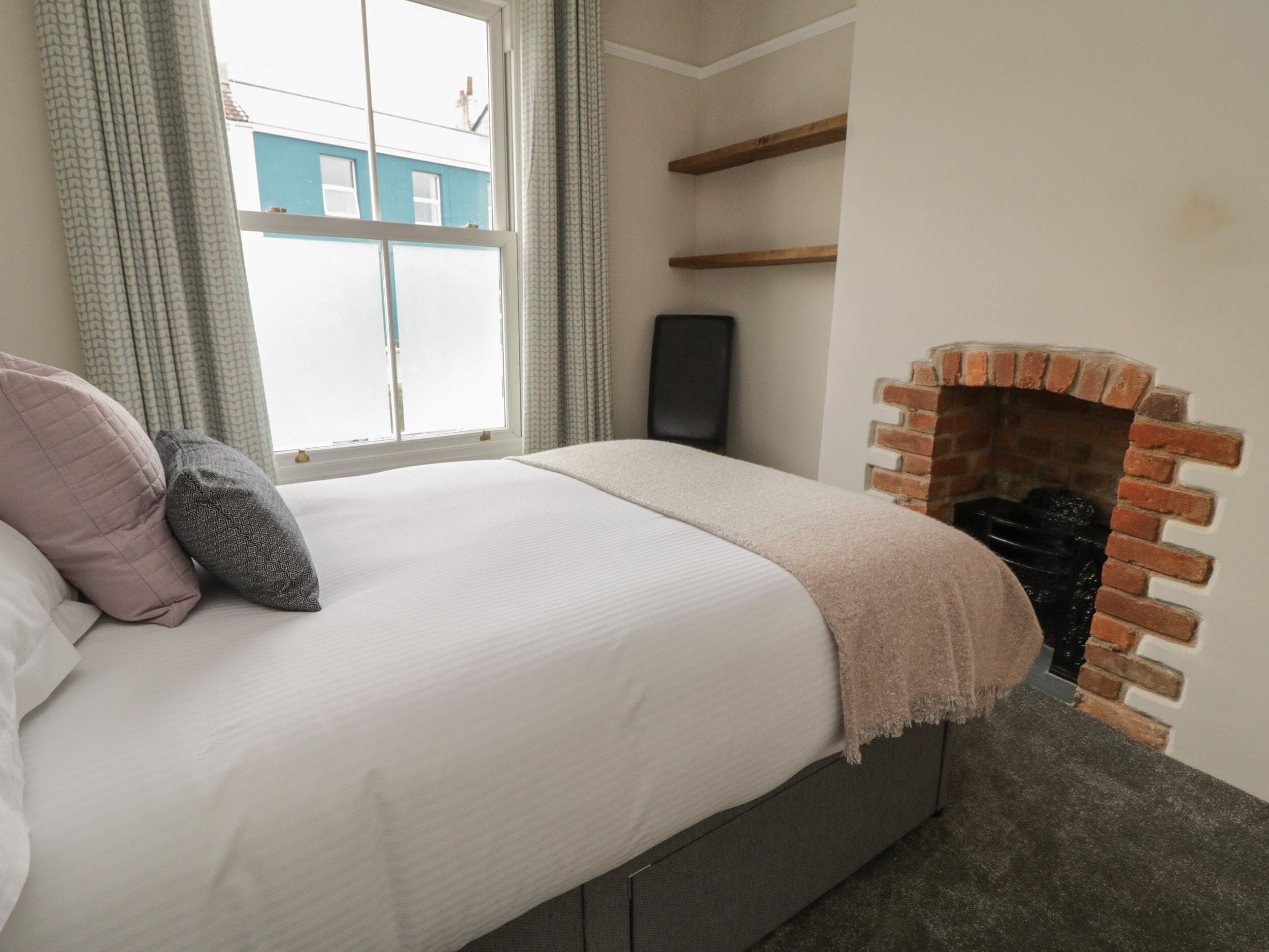 Un dormitorio con cama, chimenea, ventana y vista a un edificio.
