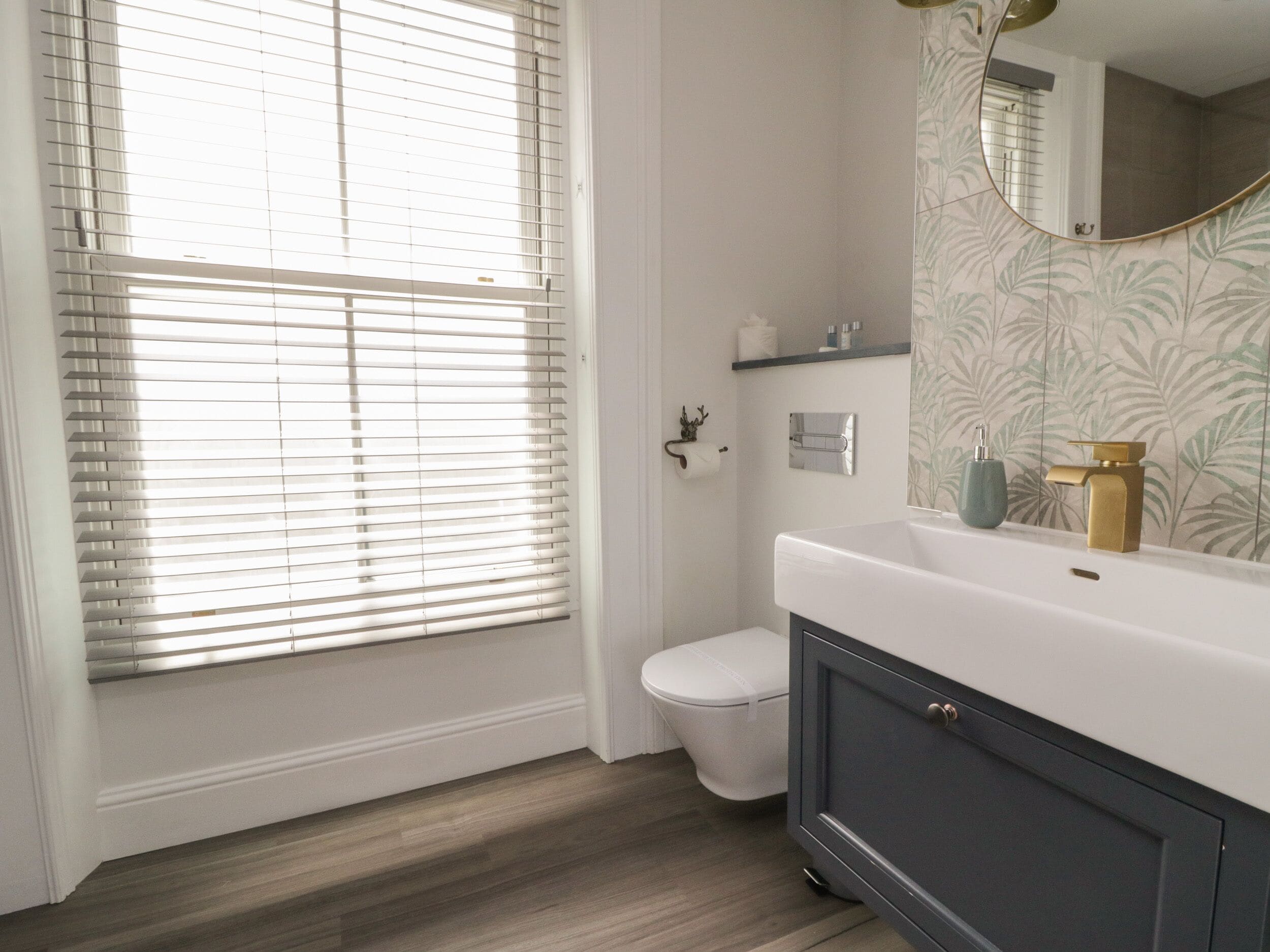 A bathroom with a toilet, a sink, and a window with blinds.