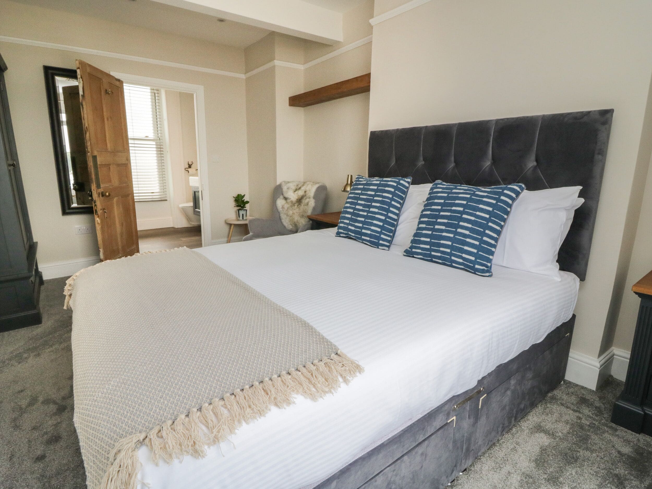 Una cama grande con cabecera oscura, ropa de cama blanca y dos almohadas estampadas.