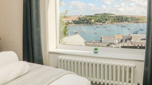 A hotel room with a view of a harbor filled with boats, a white radiator, and a bed with a white blanket.