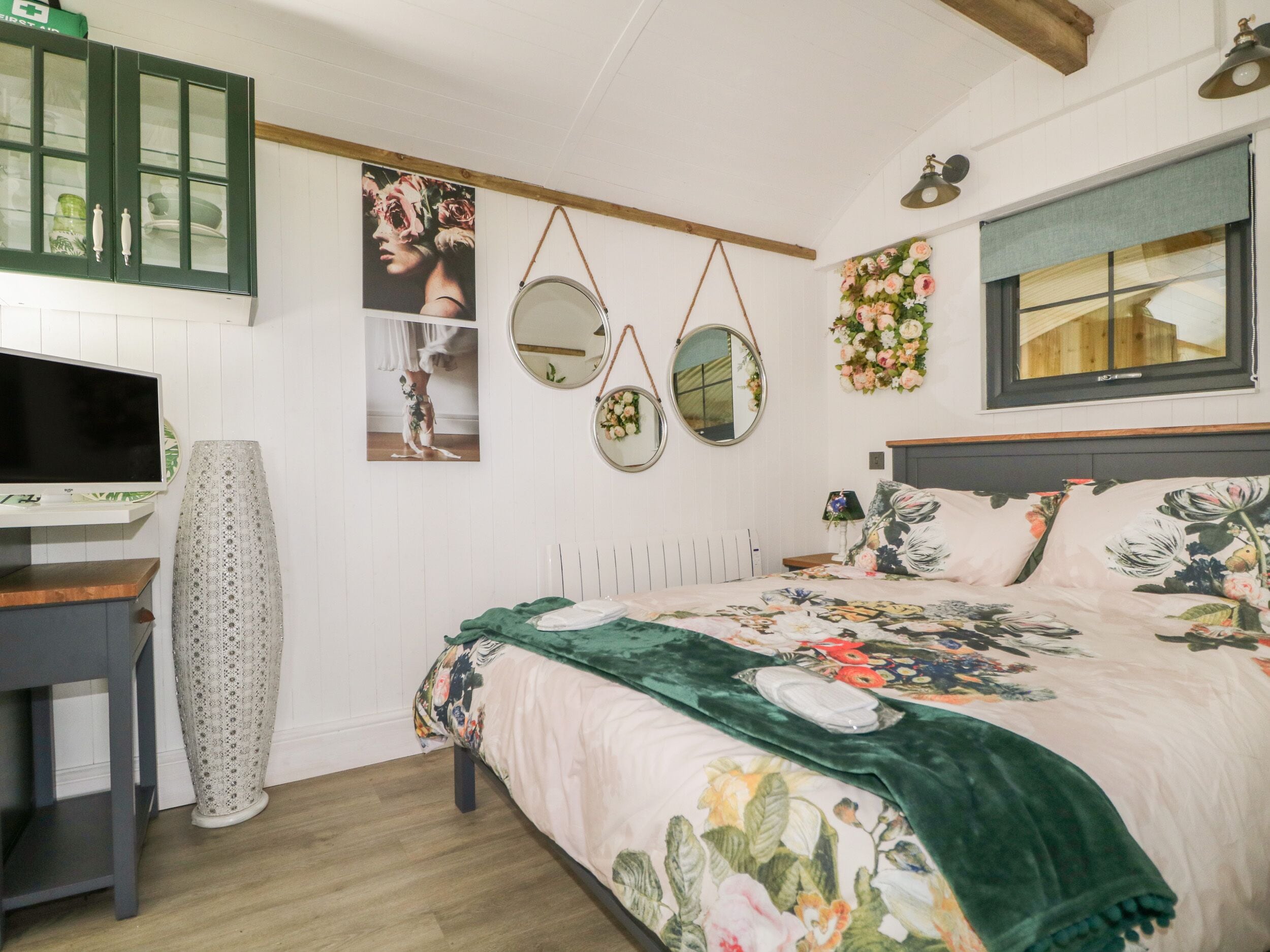 A bedroom with a bed, a desk, a television, and a mirror.