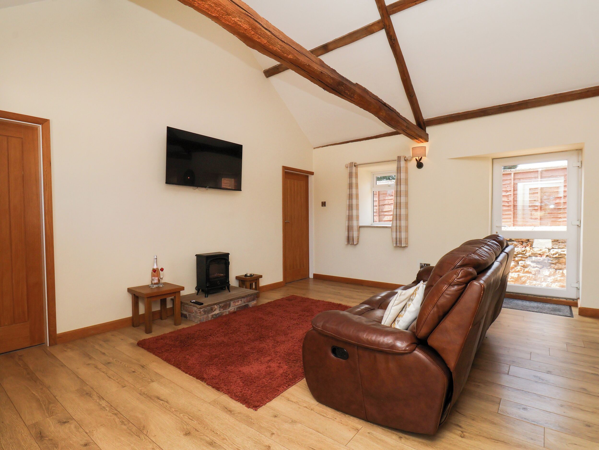 A spacious living room with a fireplace, a leather sofa, a television, and a large window with curtains.