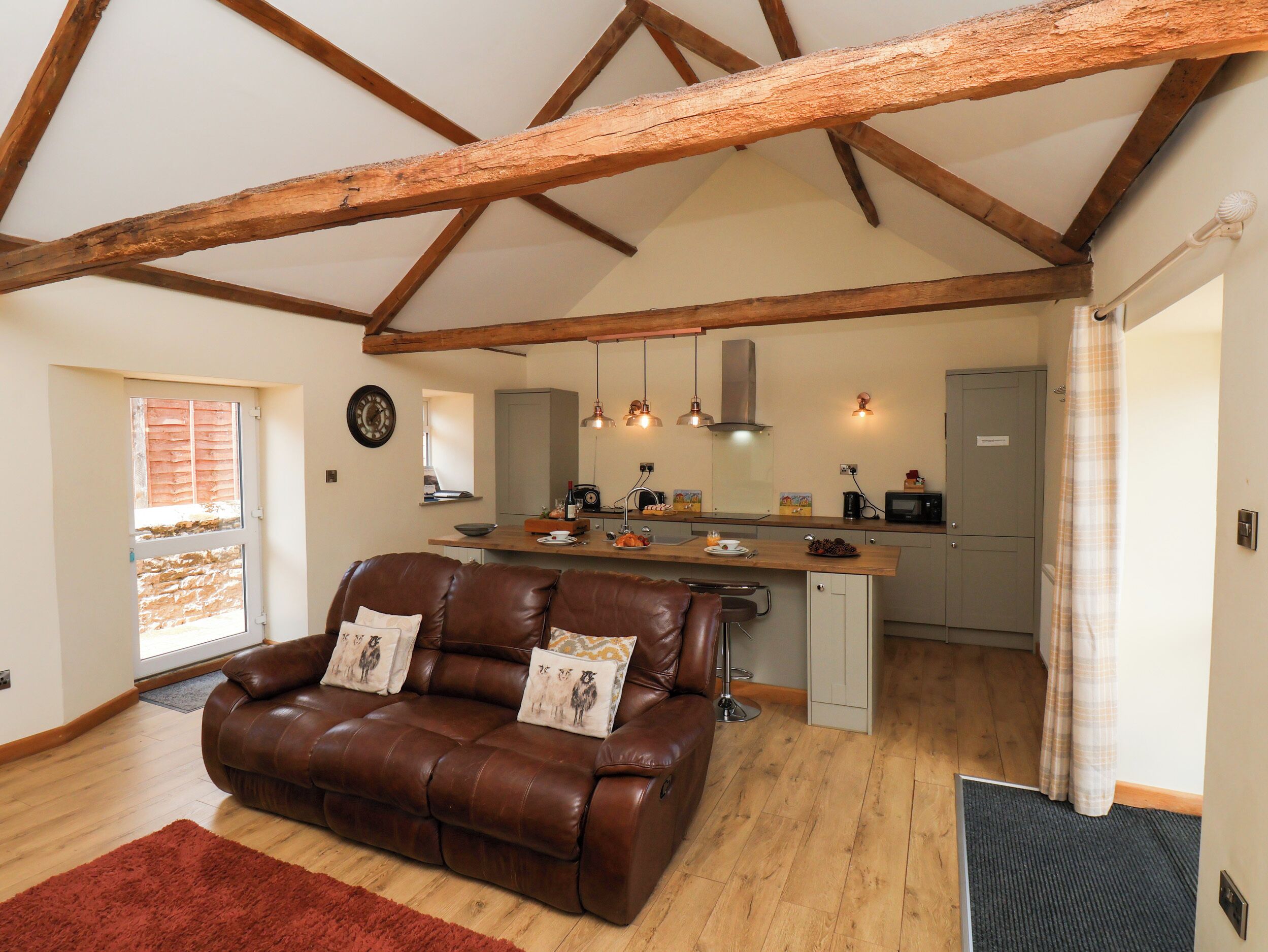 A spacious living area with a brown leather sofa, wooden beams, a kitchen with a wooden countertop, and a dining area.