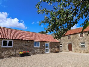 A stone building with a red-tiled roof, a gravel driveway, and a flower bed with red flowers. - Crabtree Cottage (Scarborough)