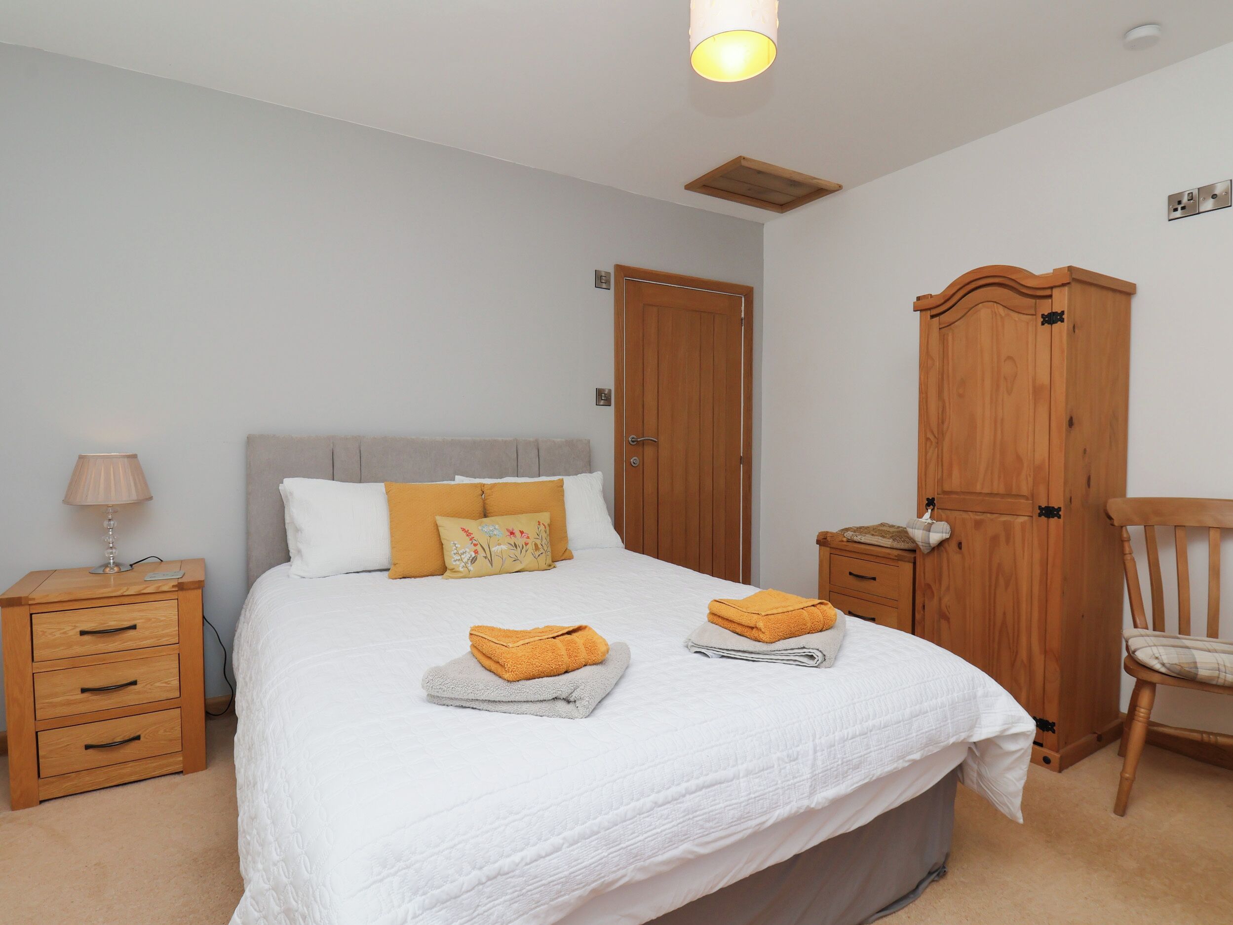 A bedroom with a bed, a nightstand, a wooden wardrobe, and a chair.