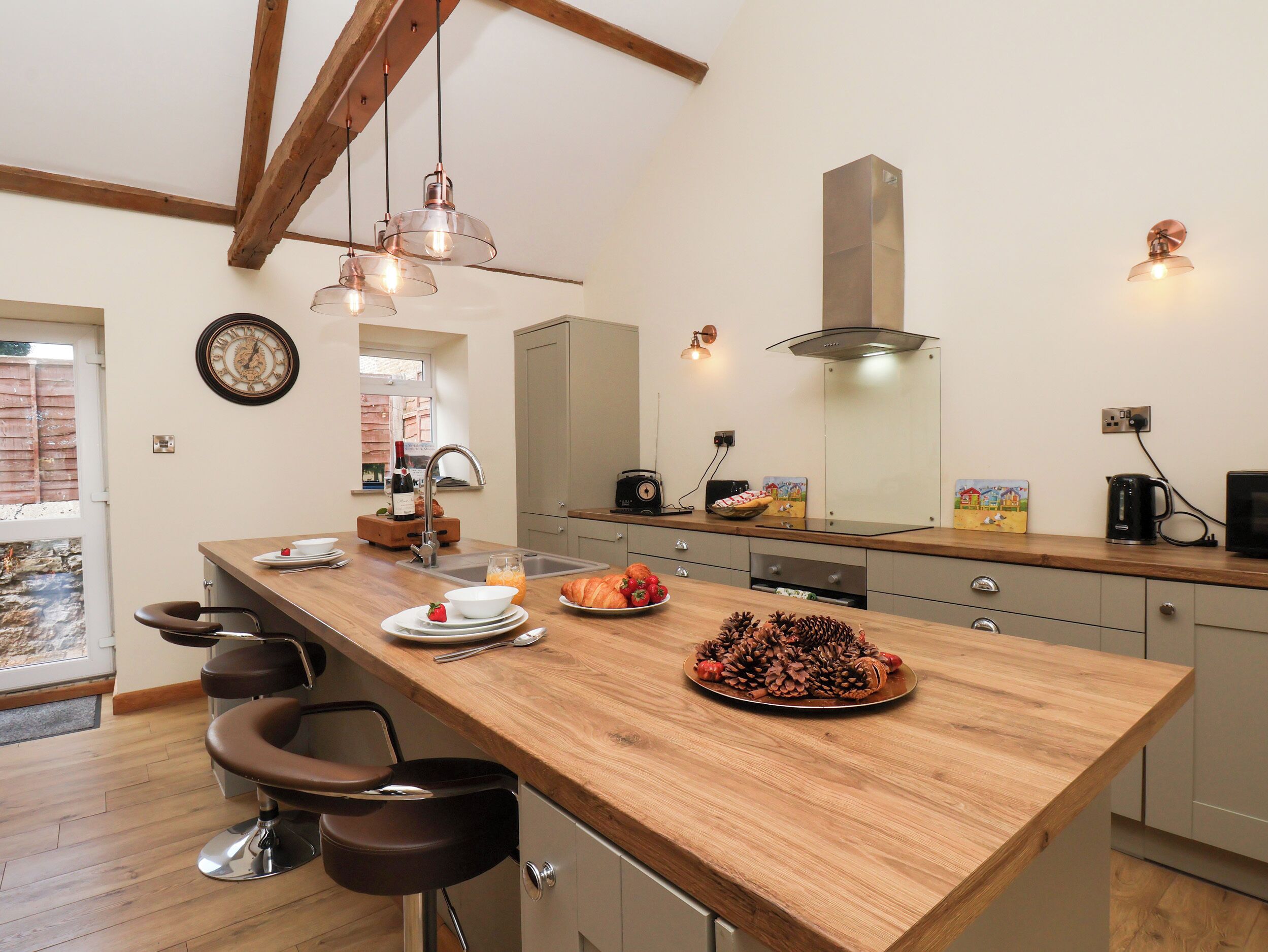 A modern kitchen with a wooden island, bar stools, a built-in oven, and pendant lighting.