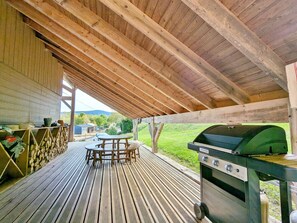 An outdoor covered patio with a wooden table and chairs, a grill, and a view of the surrounding landscape. - Charming 3-bedroom chalet with terrace near Alsace (Fraize)