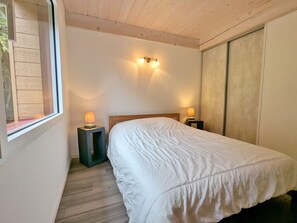 A bedroom with a bed, two bedside lamps, a window, and a wooden ceiling. - Charming 3-bedroom chalet with terrace near Alsace (Fraize)