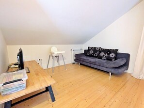 A room with a wooden table, a white chair, a grey sofa, and a black and white floral pillow. - Charming 3-bedroom chalet with terrace near Alsace (Fraize)