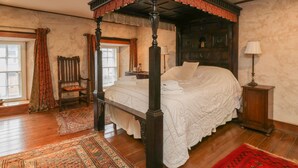 Una cama con dosel, un banco de madera, una mesita y una lámpara.