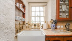 Una cocina con un lavabo, armarios de madera, una ventana y una estantería con utensilios de cocina.