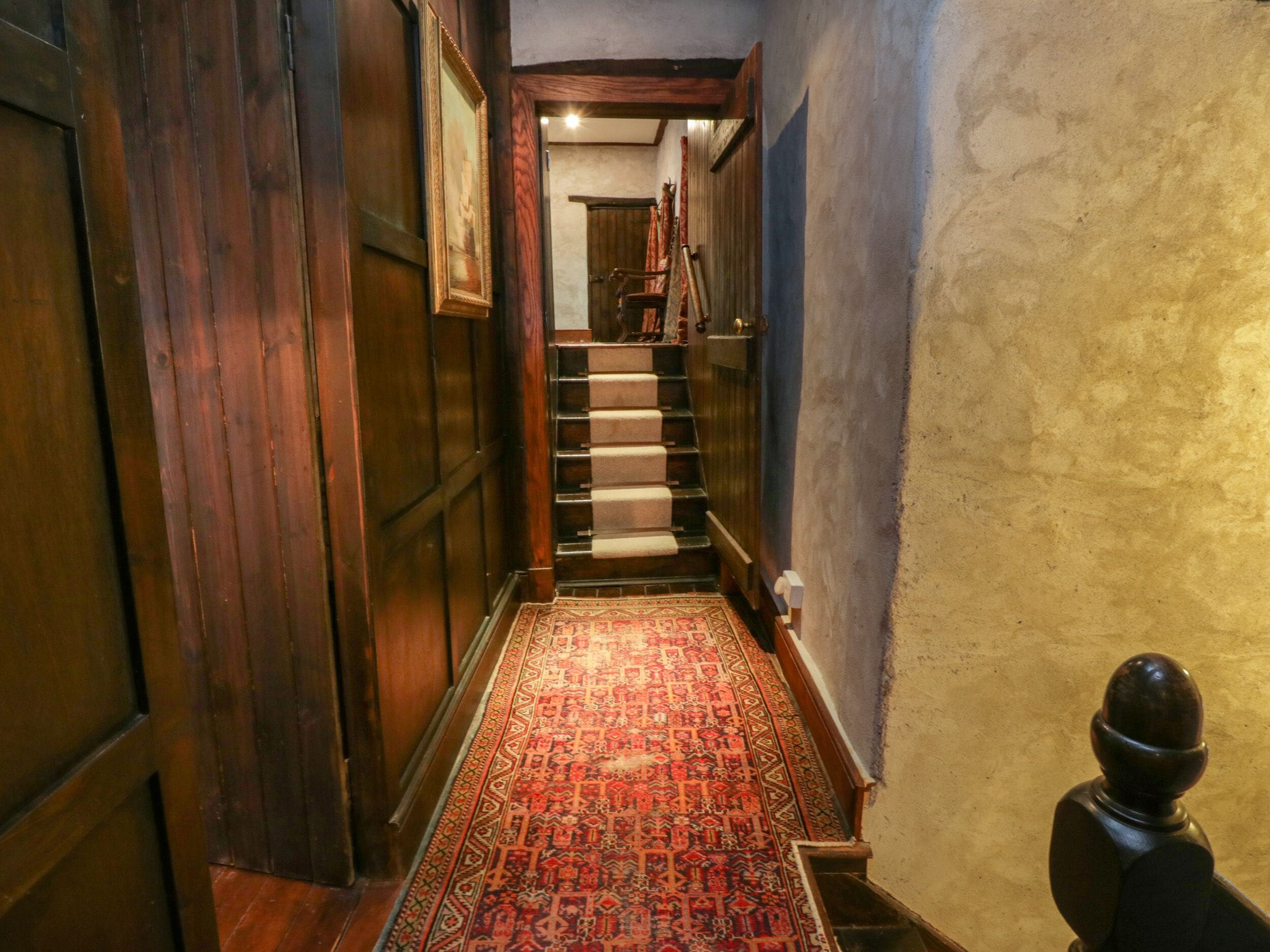A narrow hallway with a wooden door on the left, a patterned carpet, and a staircase leading to another room.
