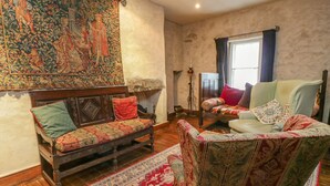 Una habitación tradicional con una cama de madera, un sofá y una silla. Hay un tapiz en la pared y una alfombra en el suelo.