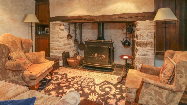 Una sala de estar acogedora con una chimenea de piedra, dos sillones, un sofá y una alfombra estampada.