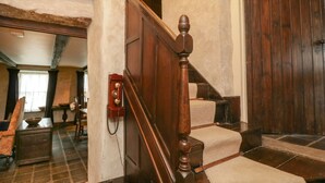 Una escalera de madera con un teléfono en la pared, que conduce a una habitación con una puerta de madera grande.