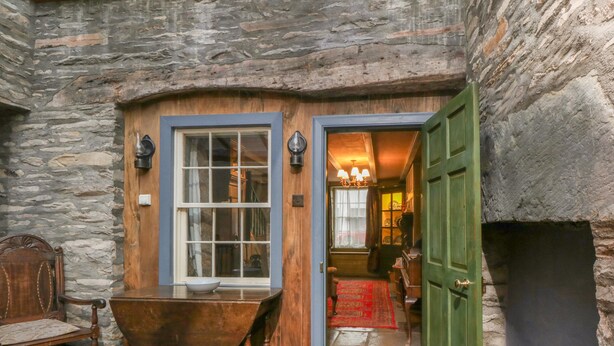 A stone-walled room with a wooden door, a large window, a wooden tub, and a red carpet. - The Precinct House (Newton Stewart)