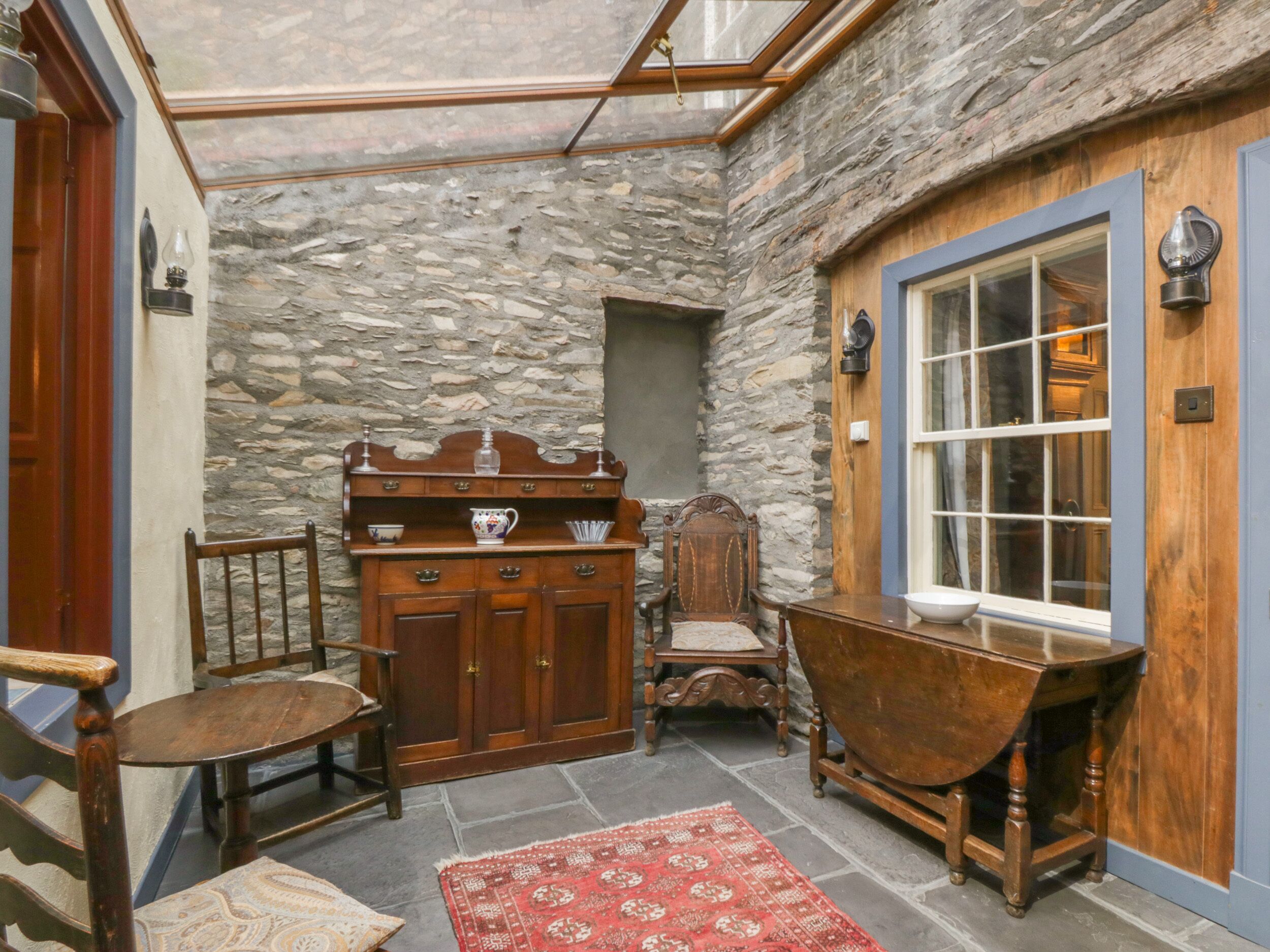 A stone-walled room with a wooden cabinet, a chair, a table, and a window.