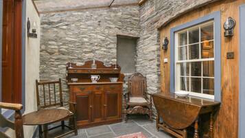 A stone-walled room with a wooden cabinet, a chair, a table, and a window.