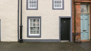 A two-story building with a cream-colored exterior and dark trim around the windows and door. - The Precinct House (Newton Stewart)