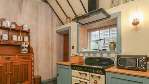 A kitchen with wooden cabinets, a stove, a microwave, and a window with a view of buildings. - The Precinct House (Newton Stewart)