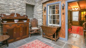 A stone-walled room with a wooden cabinet, a chair, a table, and a window with curtains. - The Precinct House (Newton Stewart)