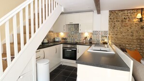 A compact kitchen with a central island, a built-in oven, and a stone accent wall. - Captain's Cottage (Sheringham)