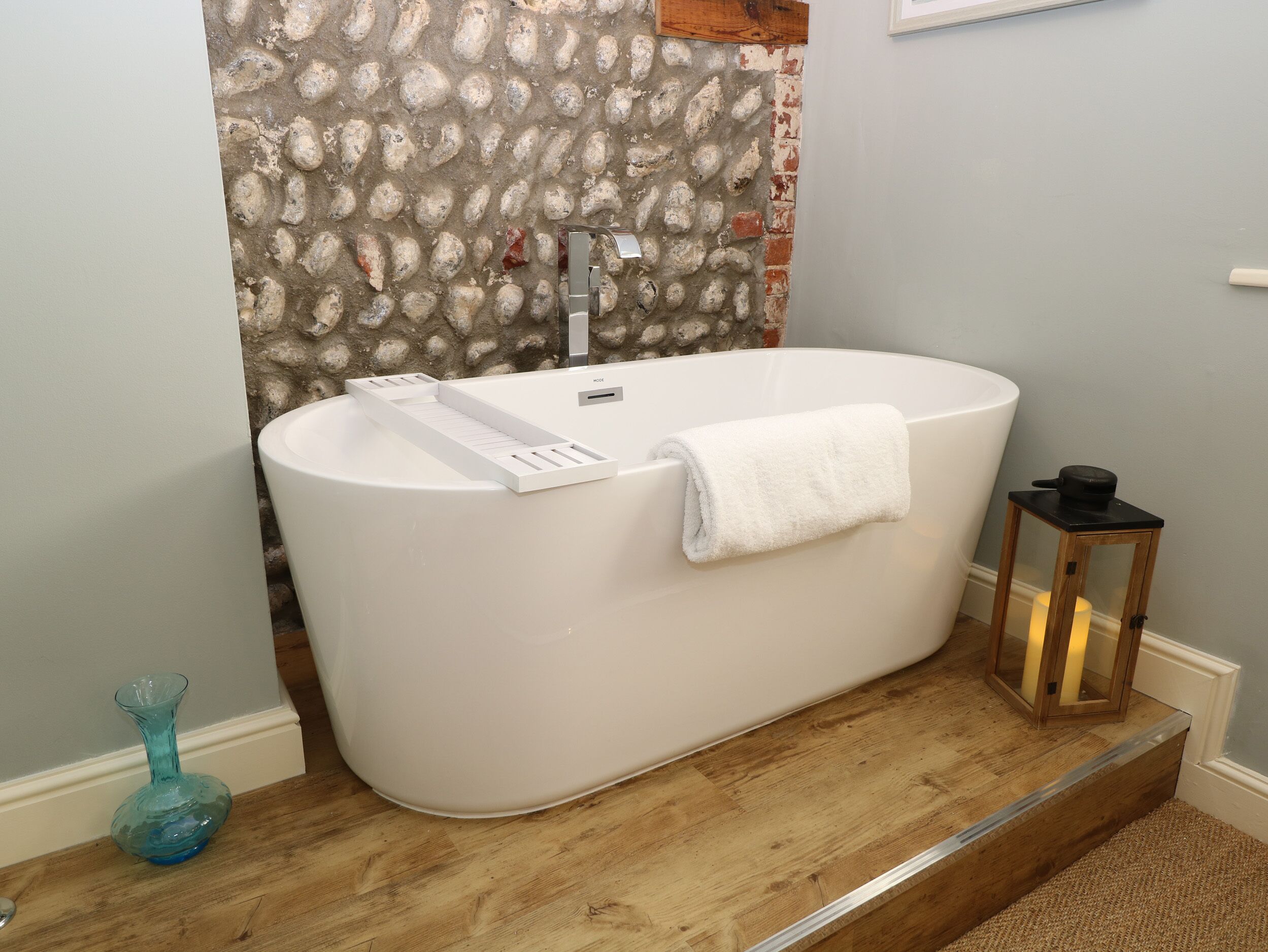 A modern bathroom with a freestanding bathtub, a glass vase, and a small wooden stool.