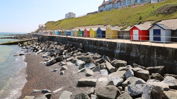 A coastal promenade with colorful beach huts and a rocky shoreline. - Captain's Cottage (Sheringham)
