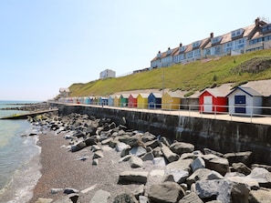 A coastal promenade with colorful beach huts and a rocky breakwater. - Captain's Cottage (Sheringham)