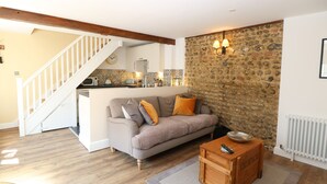 A cozy living room with a sofa, a coffee table, and a kitchen in the background. - Captain's Cottage (Sheringham)