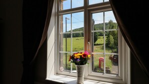 A window with a view of a green field and a red telephone box. - Lees Moor Cottage (Matlock)