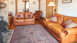 A cozy living room with a fireplace, leather sofas, a patterned rug, and wooden beams. - Lees Moor Cottage (Matlock)