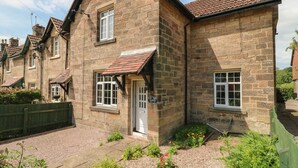 A stone cottage with a tiled roof, a front door, and a small garden with flowers. - Lees Moor Cottage (Matlock)