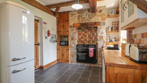 A kitchen with a stone wall backsplash, wooden cabinets, a white refrigerator, and a wooden countertop. - Lees Moor Cottage (Matlock)