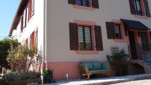 Un edificio de dos pisos con varias ventanas, un balcón y un pequeño jardín con un banco.