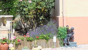 Un jardín con diversas plantas, una estatua y un elemento acuático.