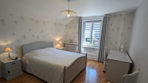 Un dormitorio con cama, mesitas de noche, una silla, una ventana con cortinas y un radiador.