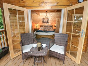 A wooden cabin with a bedroom featuring a bed, a table with chairs, and a coffee pot. - Bryn Derwen Lodge (Bangor)