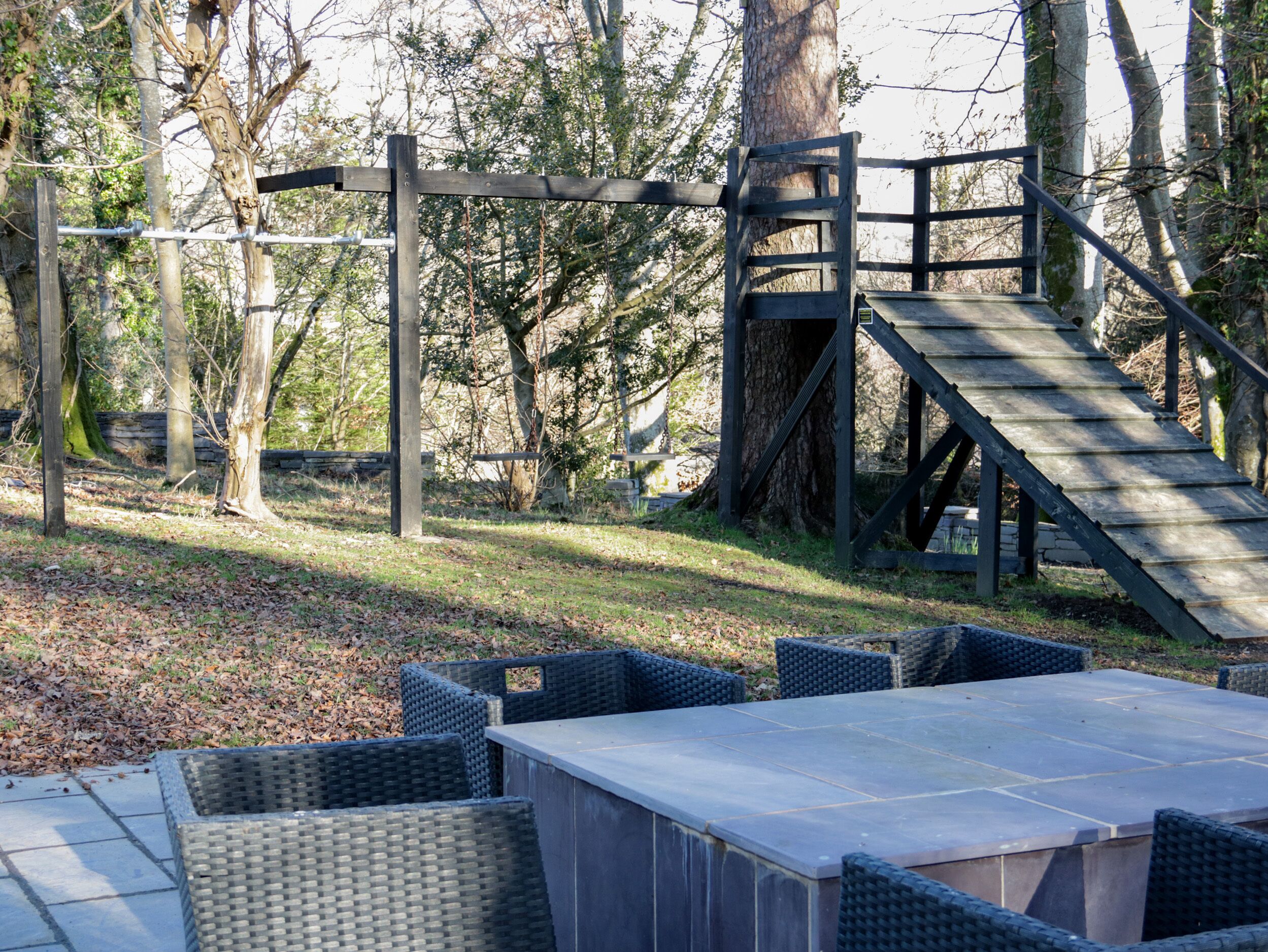 Un espace extérieur aménagé avec une table et des chaises, entouré d’arbres et agrémenté d’un escalier en bois.
