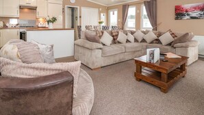 A spacious living room with a beige sofa set, a wooden coffee table, and a kitchen area in the background. - Jonstone Pines (Scarborough)
