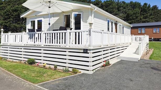A mobile home with a white exterior, a covered porch, and a small deck. - Jonstone Pines (Scarborough)