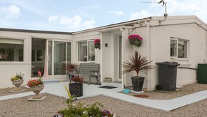 A residential building with a patio area, a bench, potted plants, and a trash bin. - Sandpiper (Dumfries)