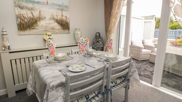 A dining area with a table set for four, a beach-themed painting on the wall, and a view of the garden through the glass door.