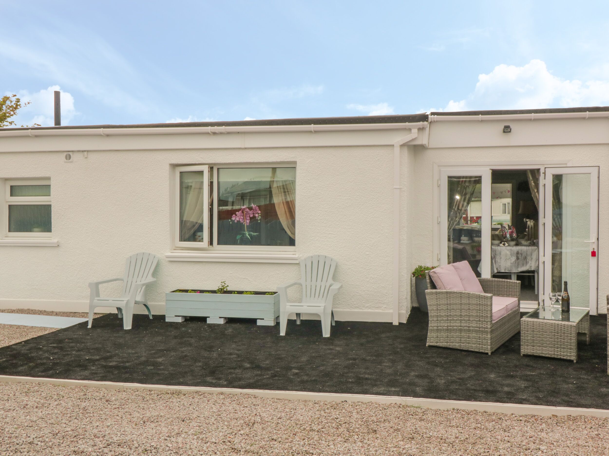 A building with a patio area featuring two white chairs, a small table, and a wicker sofa.