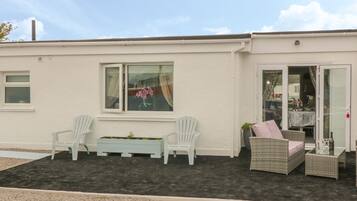 A building with a patio area featuring two white chairs, a small table, and a wicker sofa.