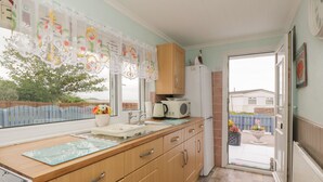 A kitchen with wooden cabinets, a microwave, a kettle, and a sink. - Sandpiper (Dumfries)