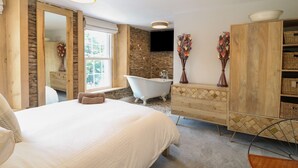 Quarto com uma cama grande, penteadeira de madeira, banheira e espelho.